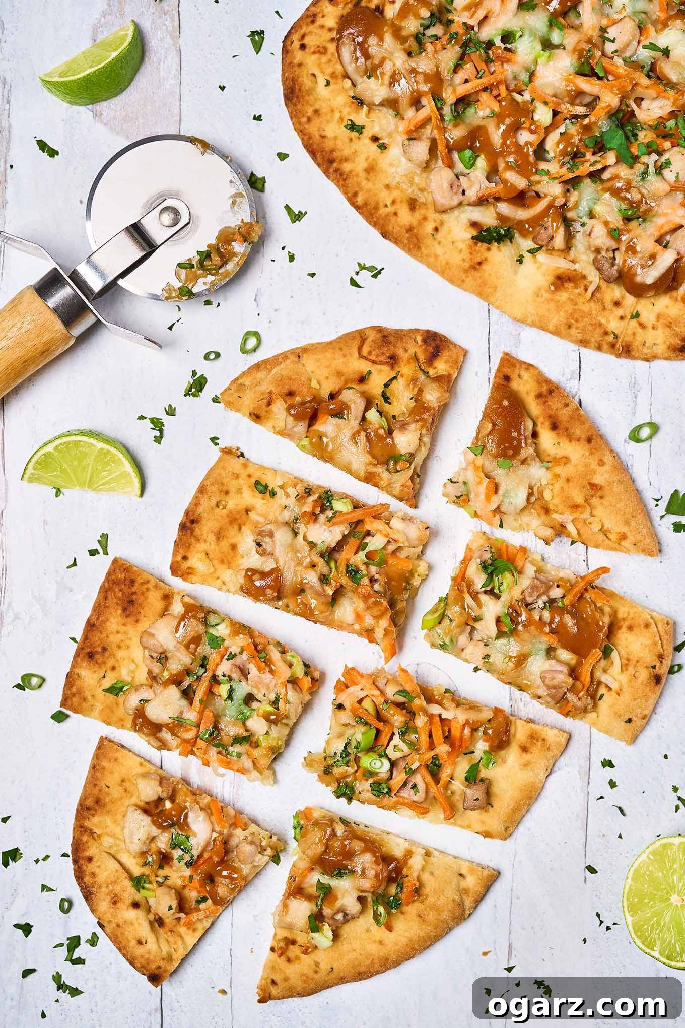 Spicy Thai Chicken Flatbread 2 Two chicken flatbread pizzas, one whole, one cut into pieces, surrounded by lime wedges and chopped cilantro, with a pizza cutter on the side.