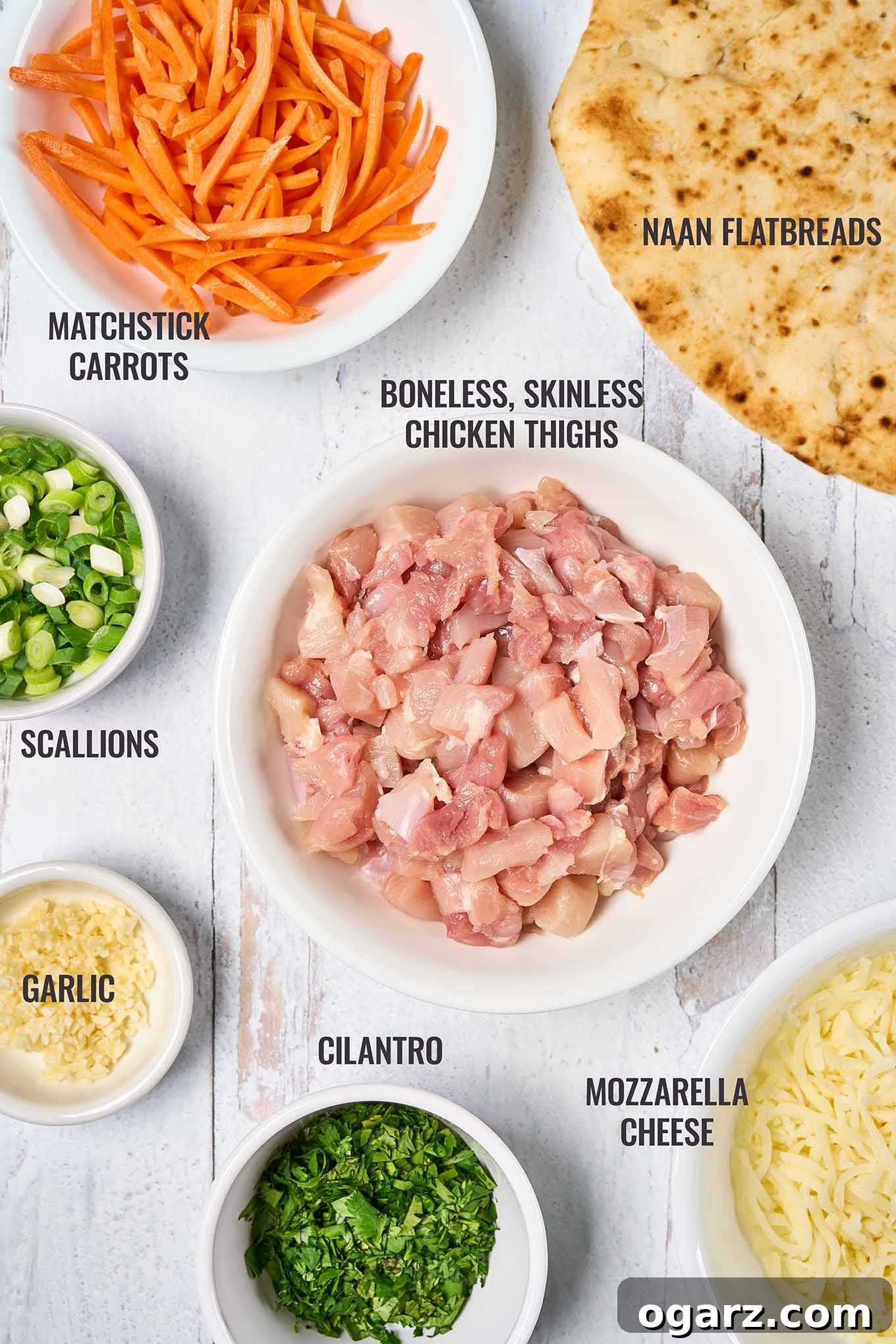 Spicy Thai Chicken Flatbread 3 A labeled, overhead view of the main ingredients needed to make Thai chicken flatbread pizzas, including cubes of chicken, naan, scallions, cilantro, and cheese.