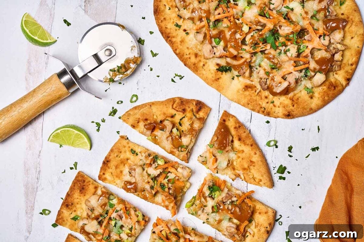Spicy Thai Chicken Flatbread 7 Two naan flatbread pizzas topped with tender chicken and vibrant Thai-style ingredients, perfectly sliced and ready to serve next to a rust colored linen napkin and wedges of fresh lime.