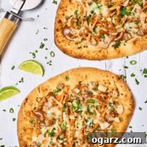 Two Thai chicken flatbread pizzas on a white wooden surface, baked and ready to be cut for serving with fresh lime wedges as garnish.