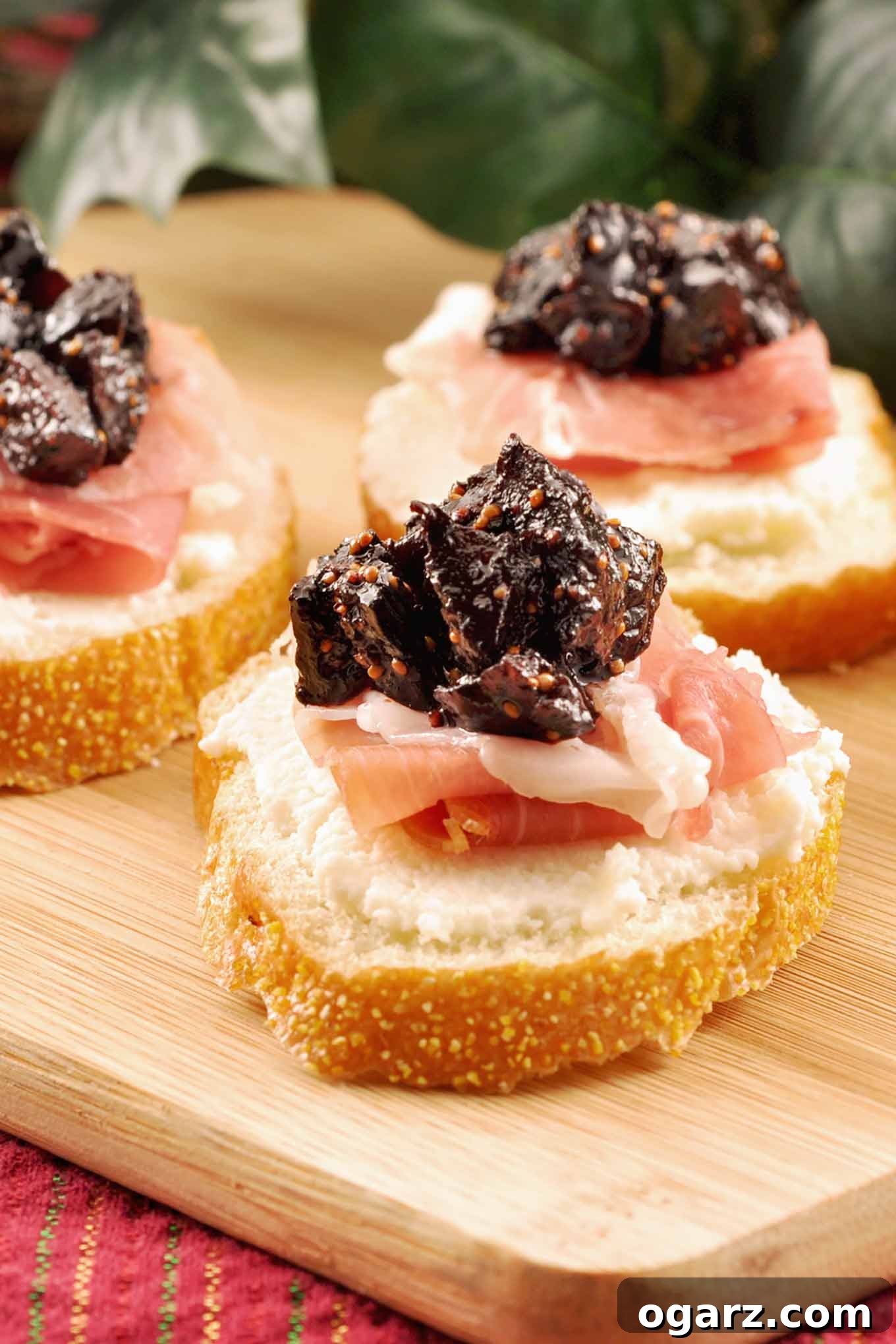 Sweet Fig Crostini with Prosciutto and Ricotta 2 Three crostini topped with whipped ricotta, prosciutto, and port wine fig compote arranged on a wooden cutting board.
