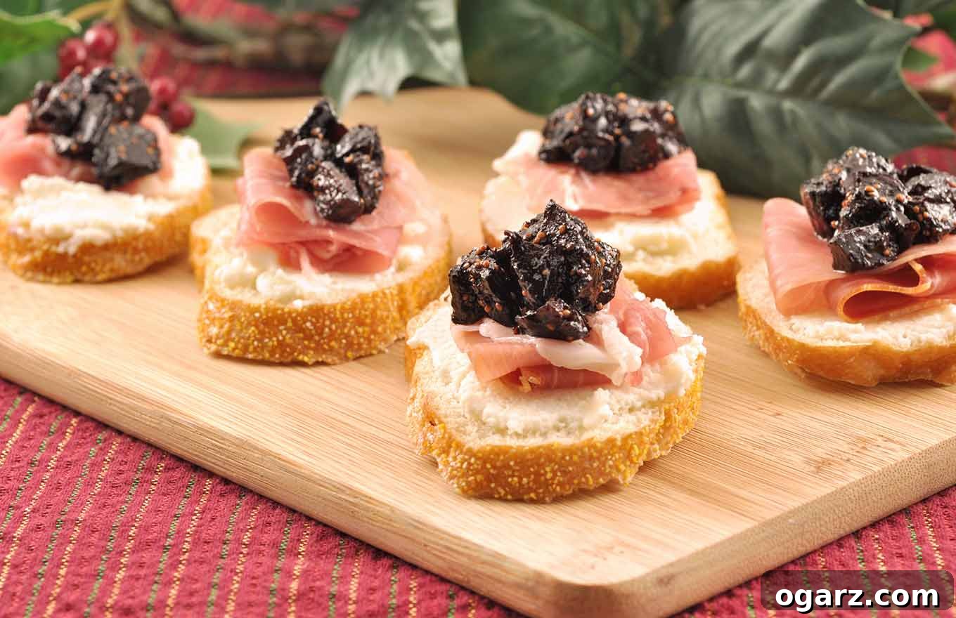 Sweet Fig Crostini with Prosciutto and Ricotta 3 Crostini topped with whipped ricotta, prosciutto, and port wine fig compote on a cutting board with Christmas table decor in the background.