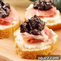 Three crostini topped with whipped ricotta, prosciutto, and port wine fig compote arranged on a wooden cutting board.