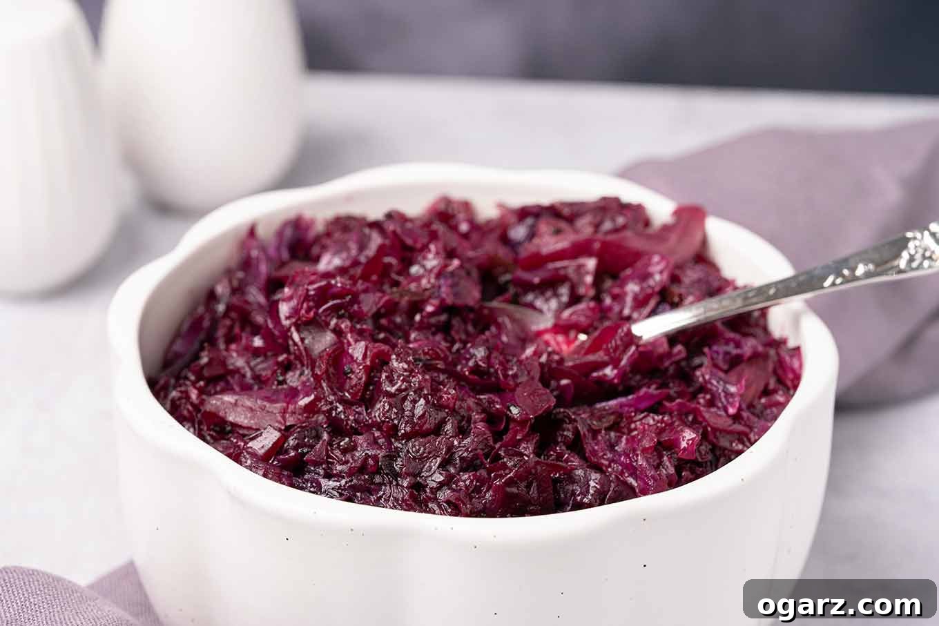 A serving bowl of red cabbage that was braised in apple cider and currant jelly with a serving spoon in it.
