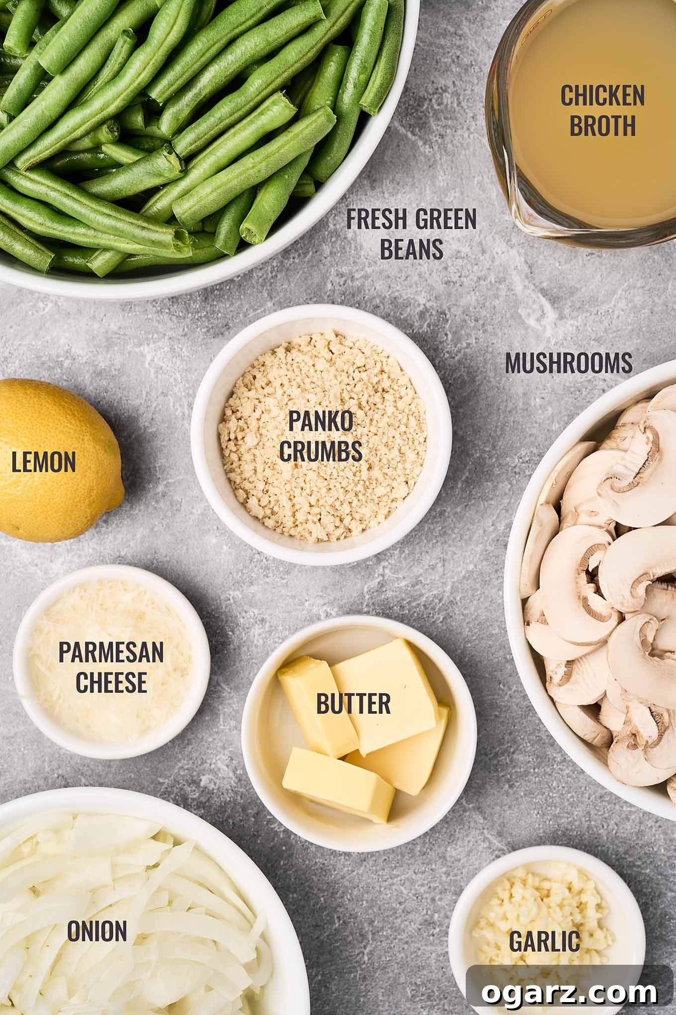 Golden Crumb Green Bean and Mushroom Medley 3 A labeled overhead photo of fresh ingredients for crumb topped green beans and mushrooms, including vibrant green beans, cremini mushrooms, panko breadcrumbs, grated Parmesan cheese, garlic cloves, and a whole onion.