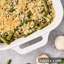 Golden Crumb Green Bean and Mushroom Medley 9 A baking dish of green beans and mushrooms with crumb topping on a gray surface with fresh, whole mushrooms and raw green beans on the side.