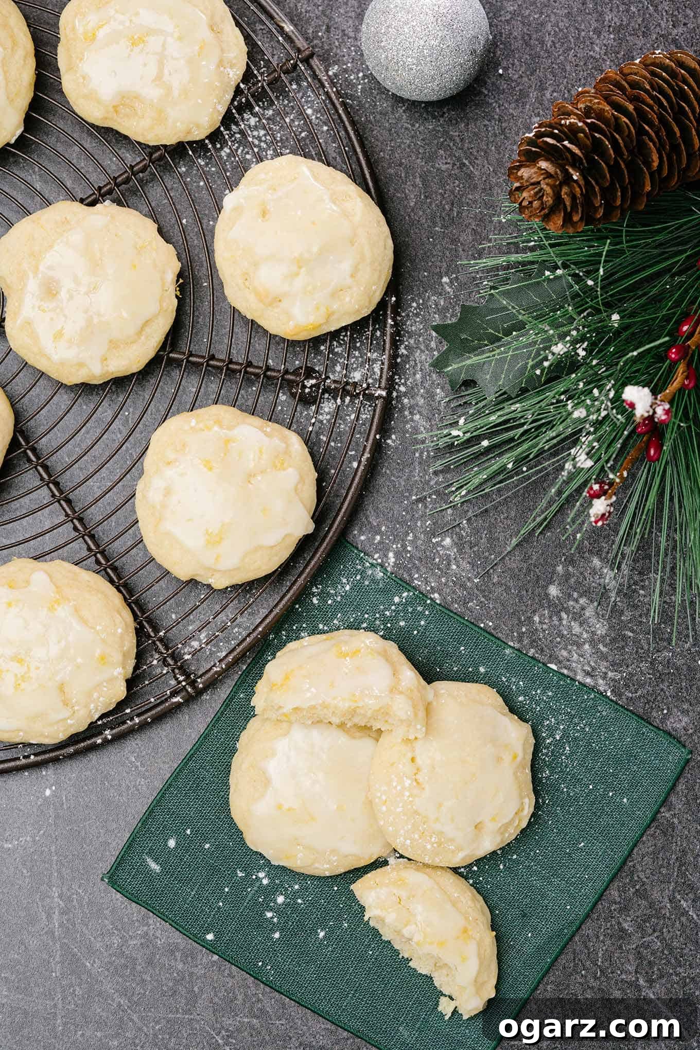An overhead view of three lemon ricotta cookies glazed and sprinkled with powdered sugar on a linen napkin, a cooling rack with more cookies to the left.