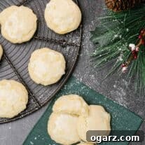 An overhead view of three lemon ricotta cookies glazed and sprinkled with powdered sugar on a linen napkin, a cooling rack with more cookies to the left.