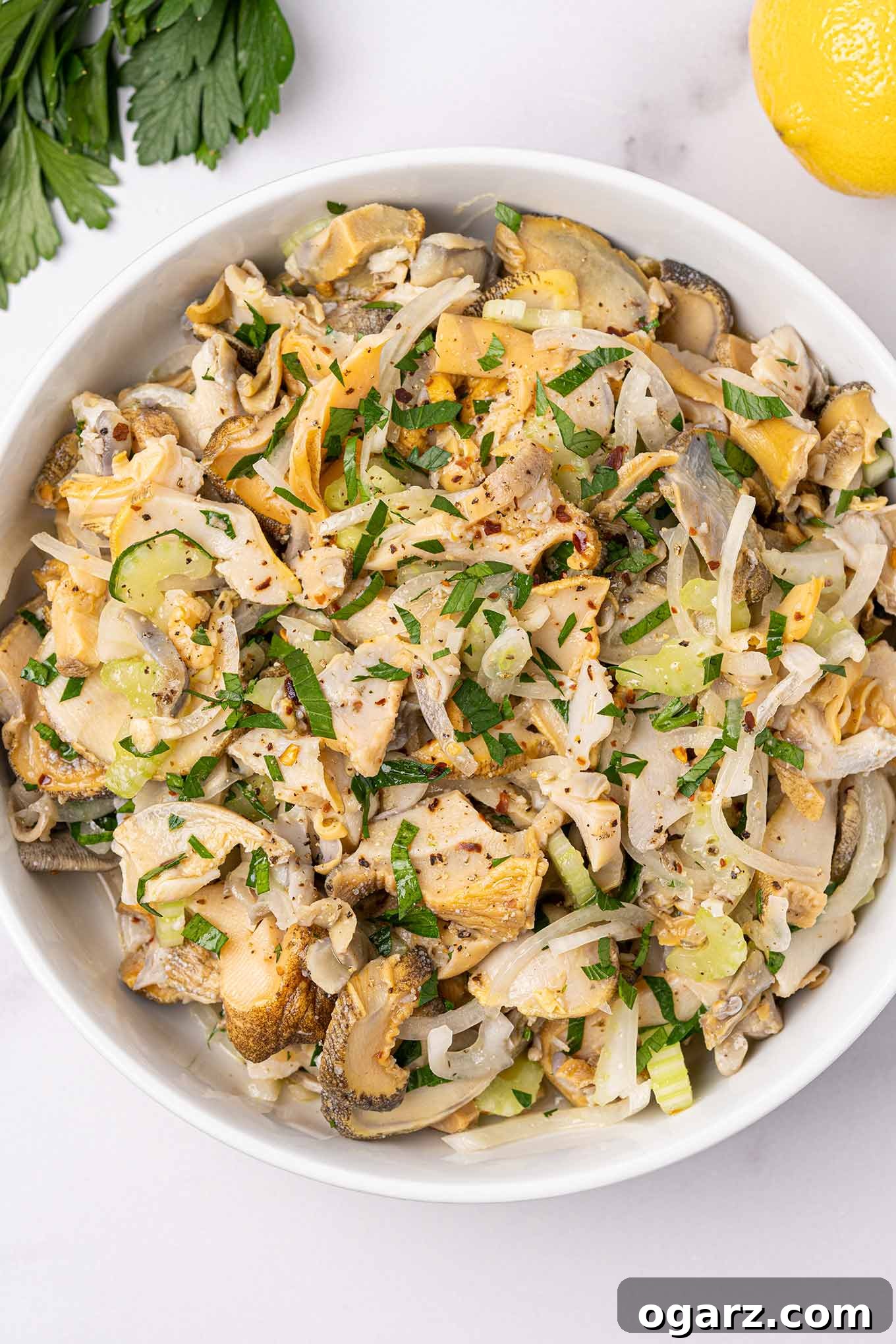 Scungilli salad in a bowl, featuring tender sea snails, diced celery, onion, and a sprinkle of red pepper flakes for a touch of heat.