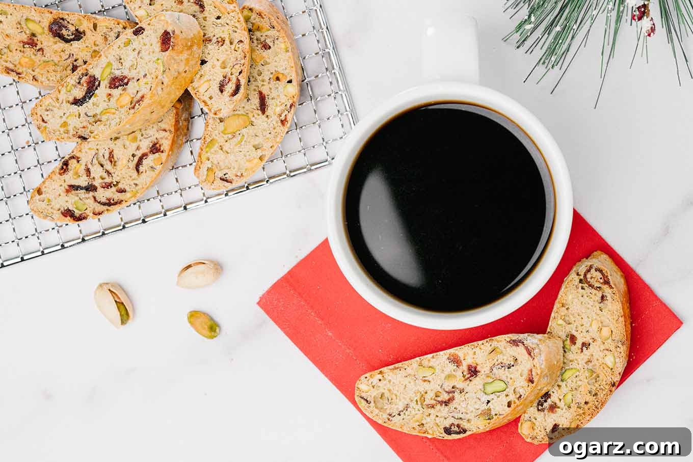 Pistachio & Cranberry Biscotti 3 An overhead view of a cranberry pistachio biscotti on a cooling rack next to a cup of coffee and two biscotti on a red napkin, showcasing its perfect crispness.