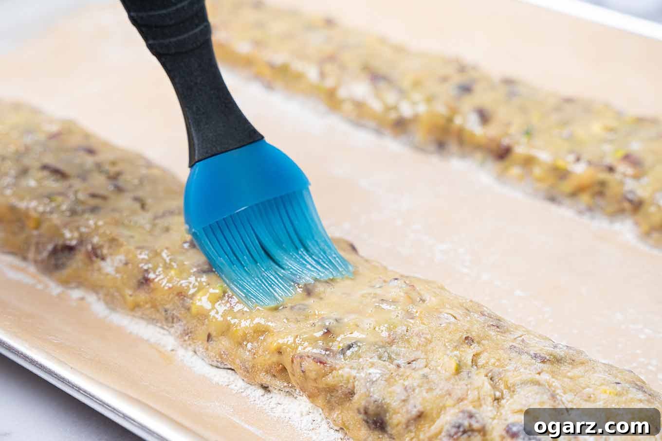 Pistachio & Cranberry Biscotti 4 Cranberry pistachio biscotti dough on a baking sheet, being brushed with beaten egg prior to first baking.