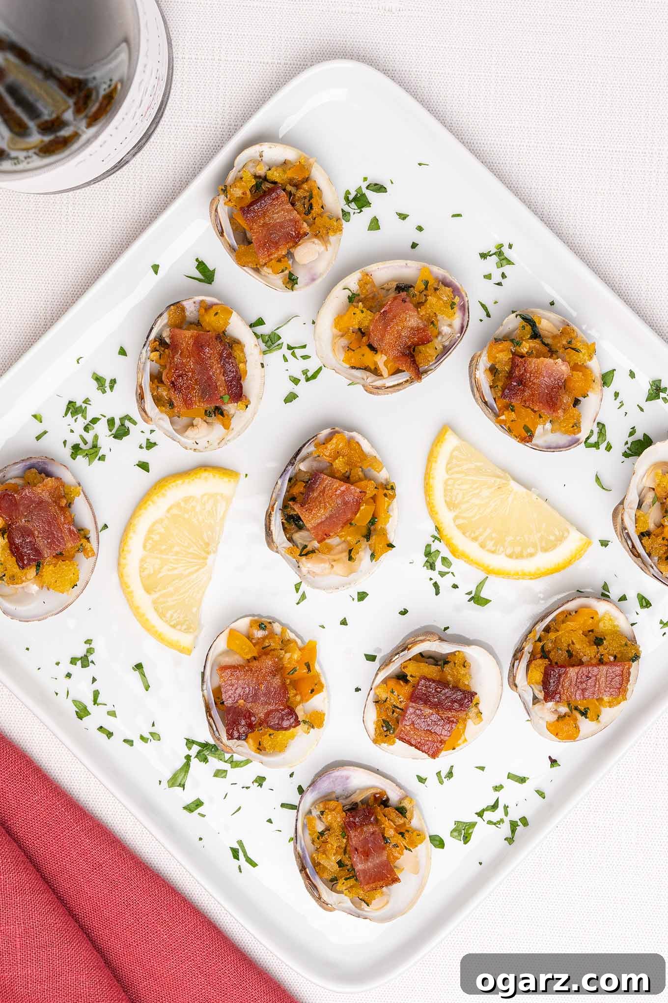 Classic New England Clams Casino 2 Clams Casino topped with crispy bacon, fresh parsley, and bright lemon wedges, artfully arranged on an appetizer serving plate.