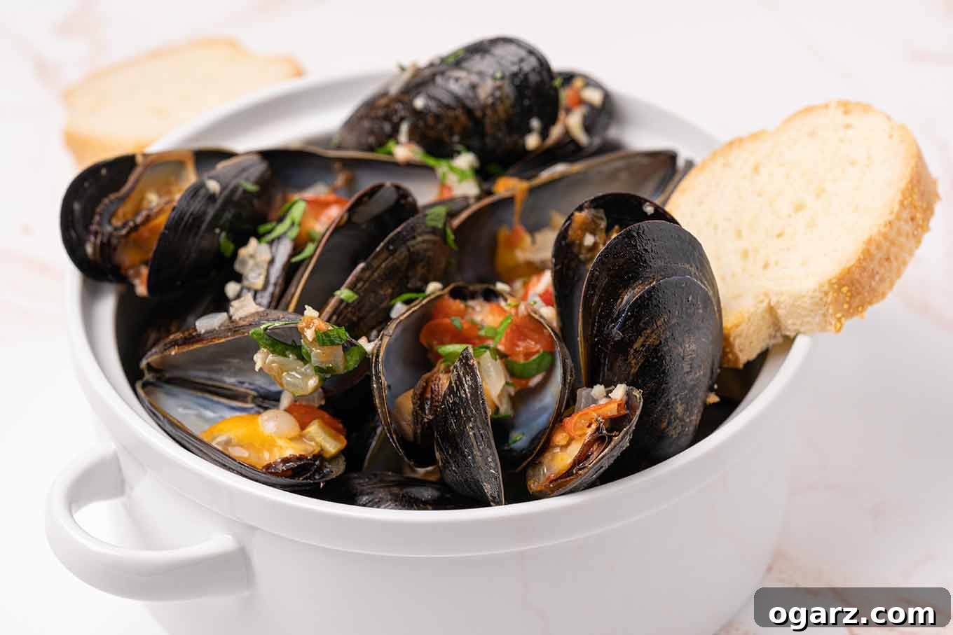 Mussels Italia 4 A serving bowl filled with steamed mussels topped with bits of garlic, onion, tomato, and parsley and crusty bread for dipping.