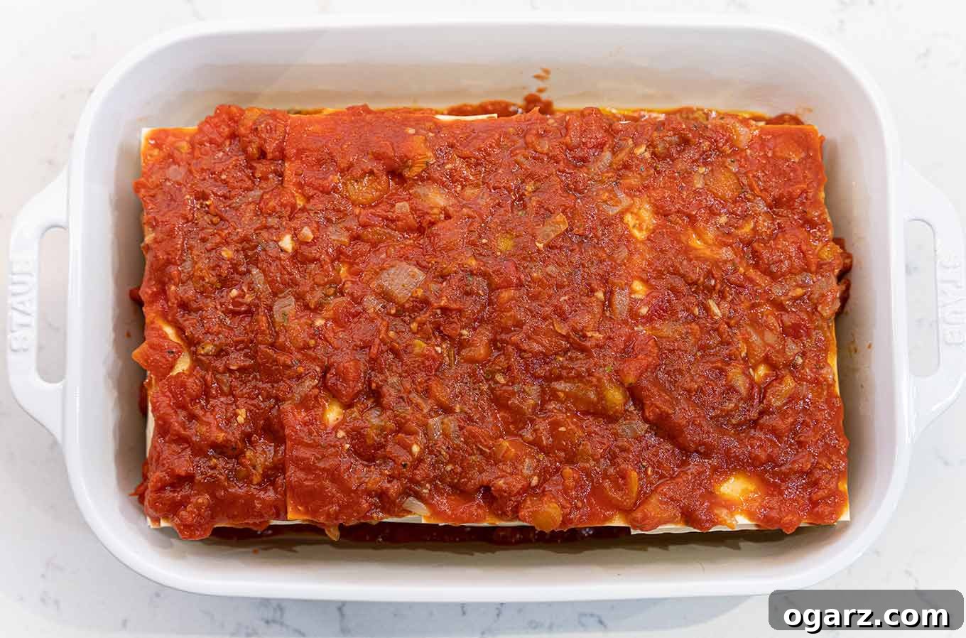 Hearty Sausage Lasagna 4 A white ceramic lasagna pan filled with a fully assembled lasagna and ready for the oven. Layers are visible, promising a delicious outcome.