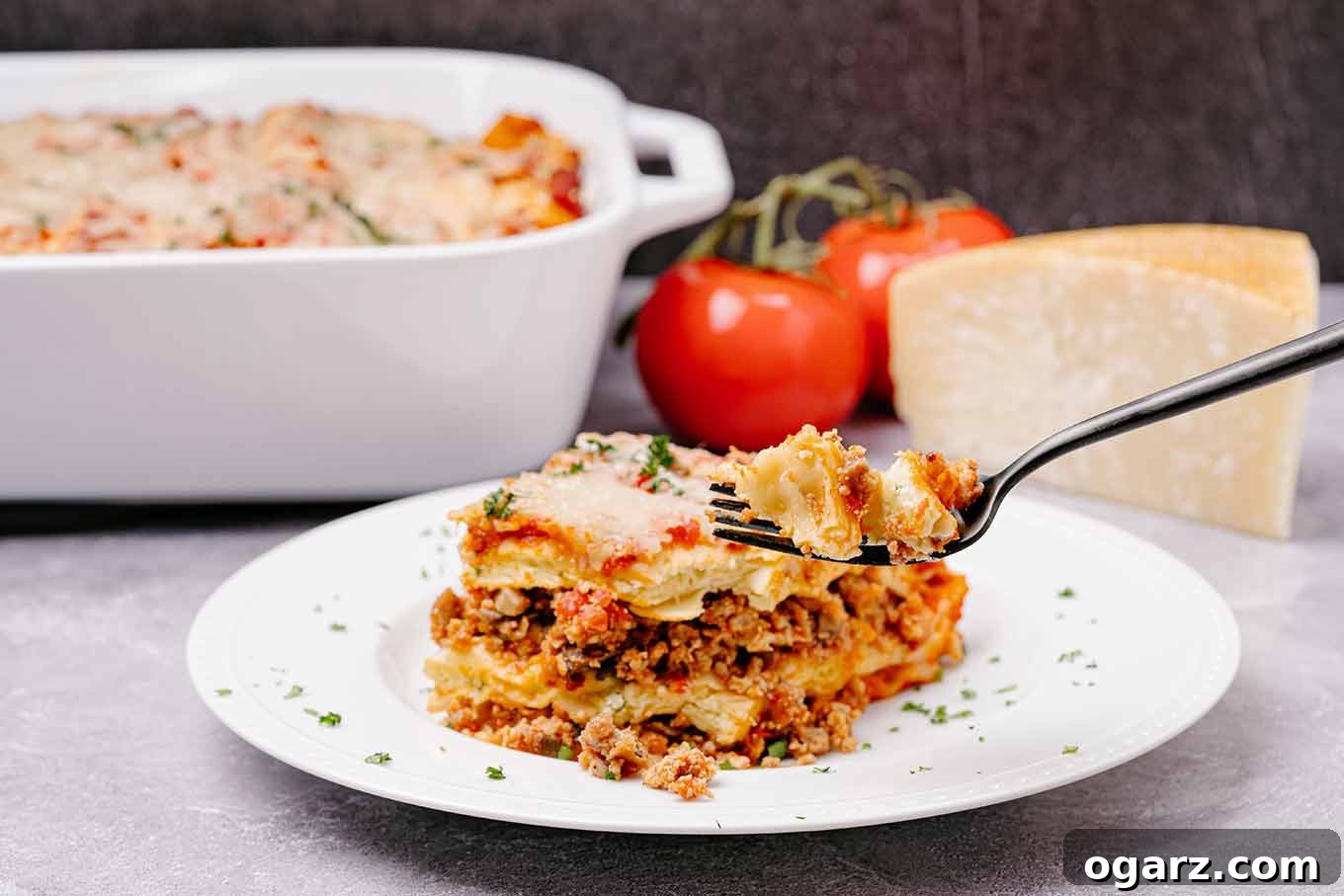 Hearty Sausage Lasagna 6 A serving of sausage lasagna with a forkful being held up, lasagna pan, whole tomatoes, and a wedge of Parmesan in the background. A culinary delight.