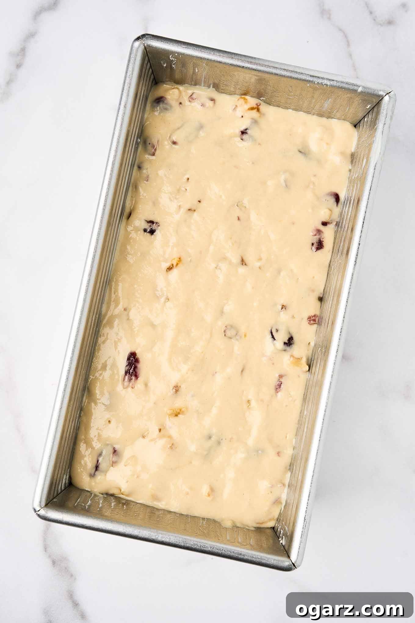 Golden Apricot Cranberry Loaf 5 Unbaked batter for apricot quick bread with cranberries and walnuts spread evenly in a greased metal loaf pan, ready for the oven.