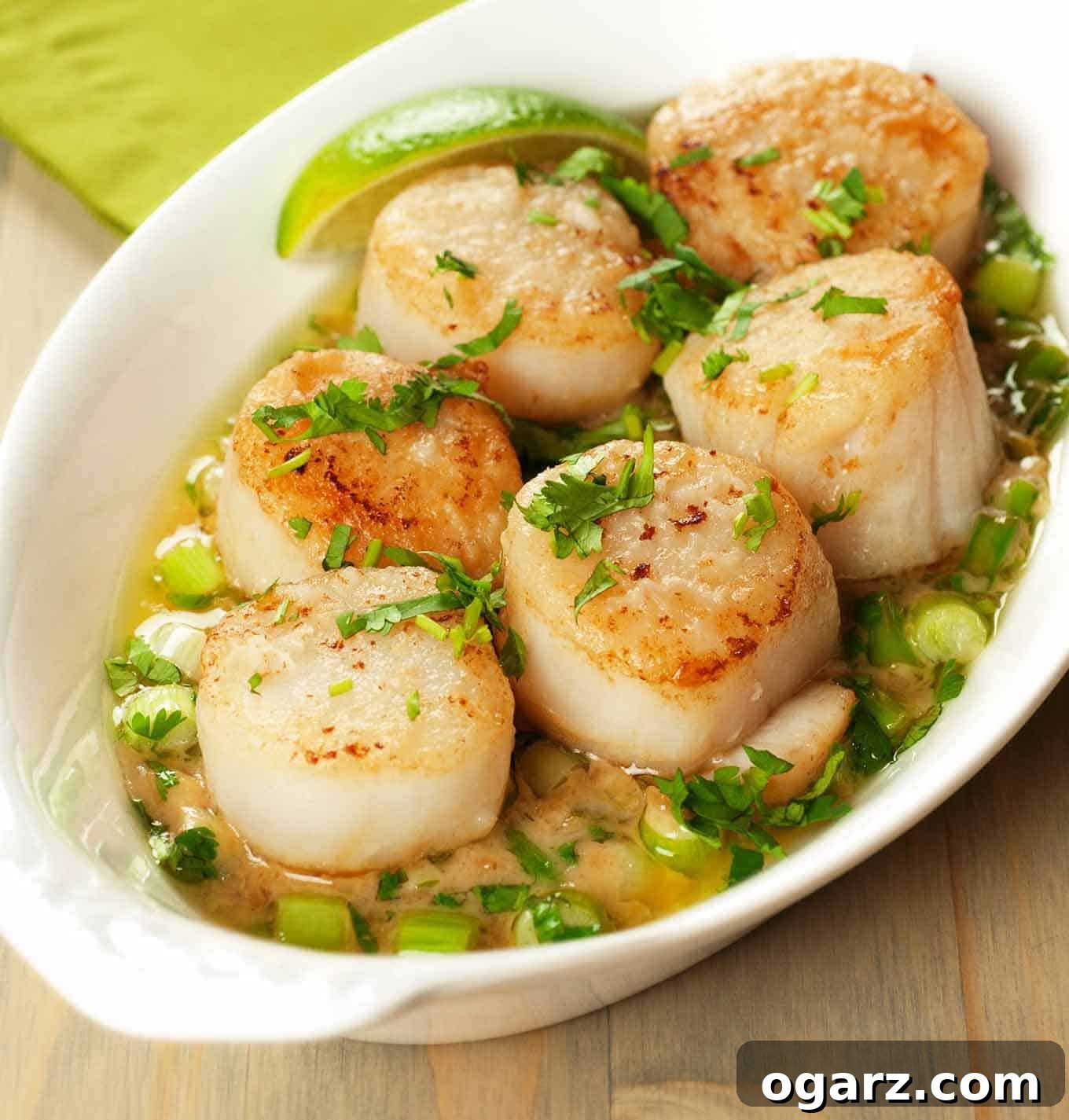 An oval dish of pan-seared sea scallops in a creamy, buttery sauce of fresh ginger, garlic, and lime, garnished with fresh cilantro.