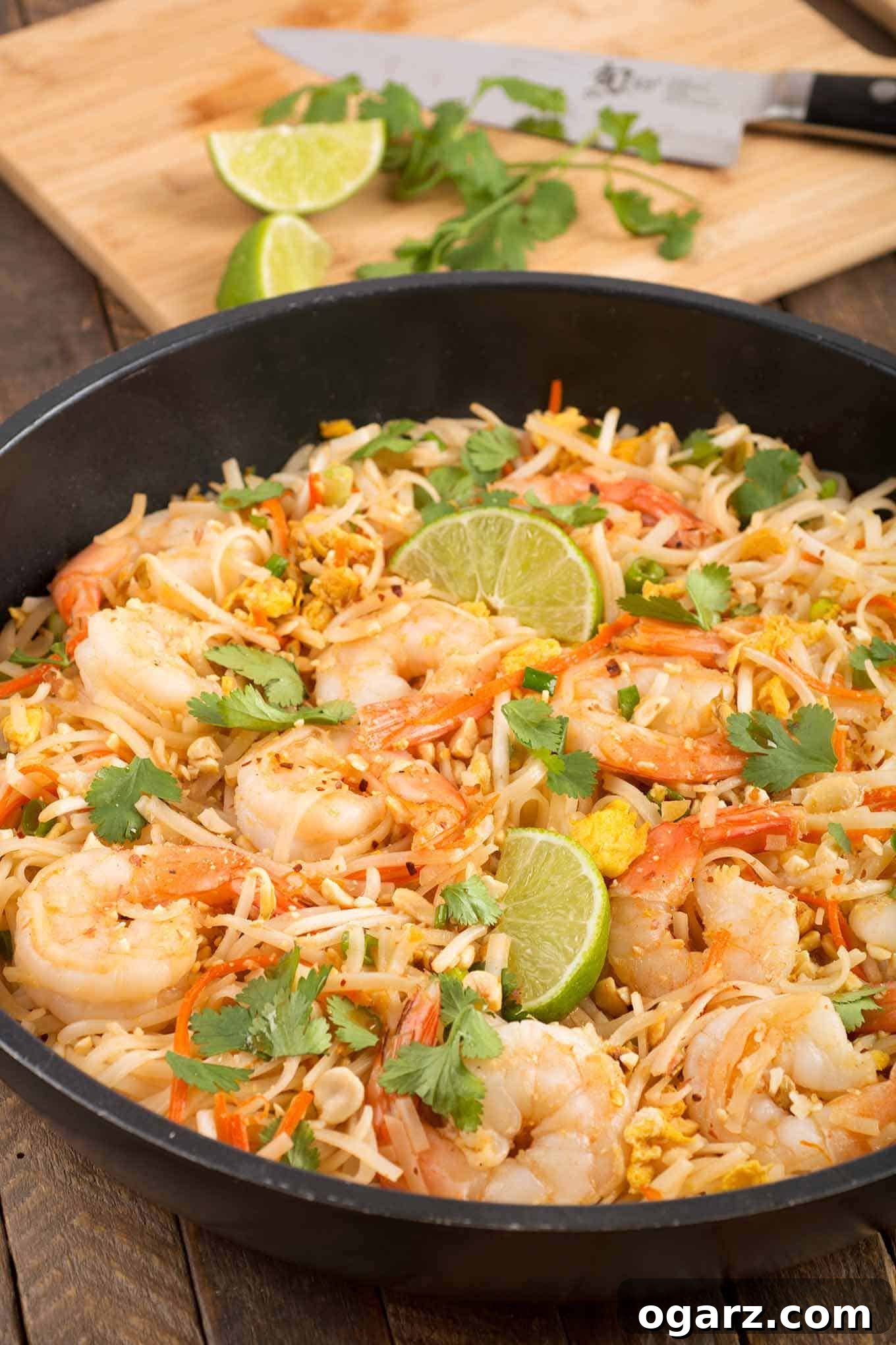 Classic Shrimp Pad Thai Delight 2 Vibrant Shrimp Pad Thai noodles in a sauté pan, garnished with fresh lime wedges and cilantro. Extra lime and cilantro are visible on a cutting board in the background, suggesting fresh ingredients.