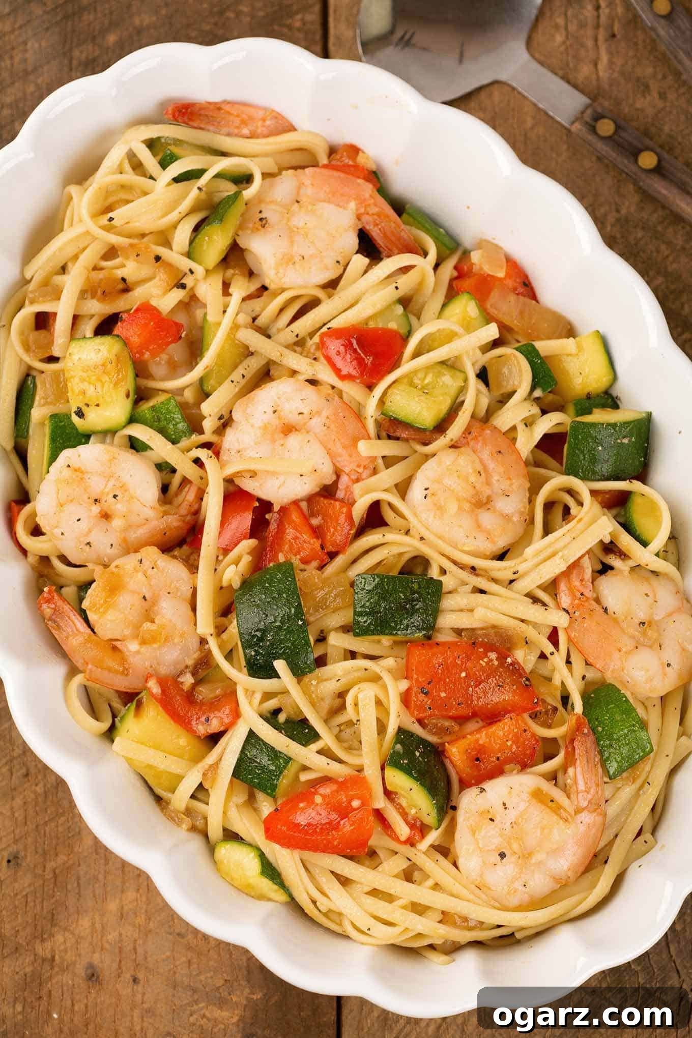 An overhead view of an oval casserole filled with sautéed zucchini and red bell pepper tossed in a light garlic sauce with linguine and shrimp.