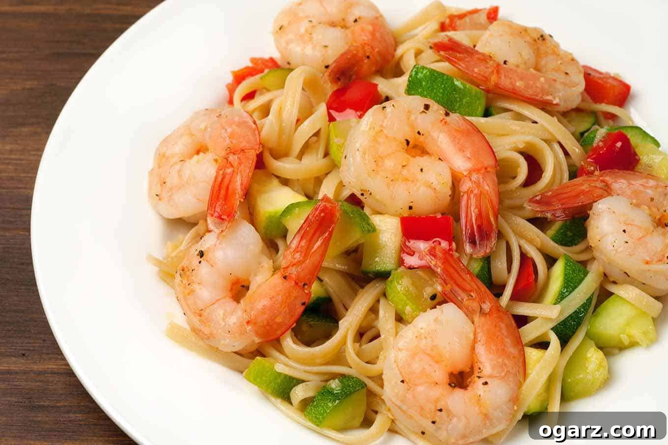 An overhead view of a plate of linguine combined with sautéed shrimp, zucchini, and red bell pepper.
