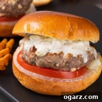 Grecian Lamb & Herb Burgers 6 A serving board with a grilled lamb burger on a brioche bun with tzatziki sauce and slices of onion and tomato.