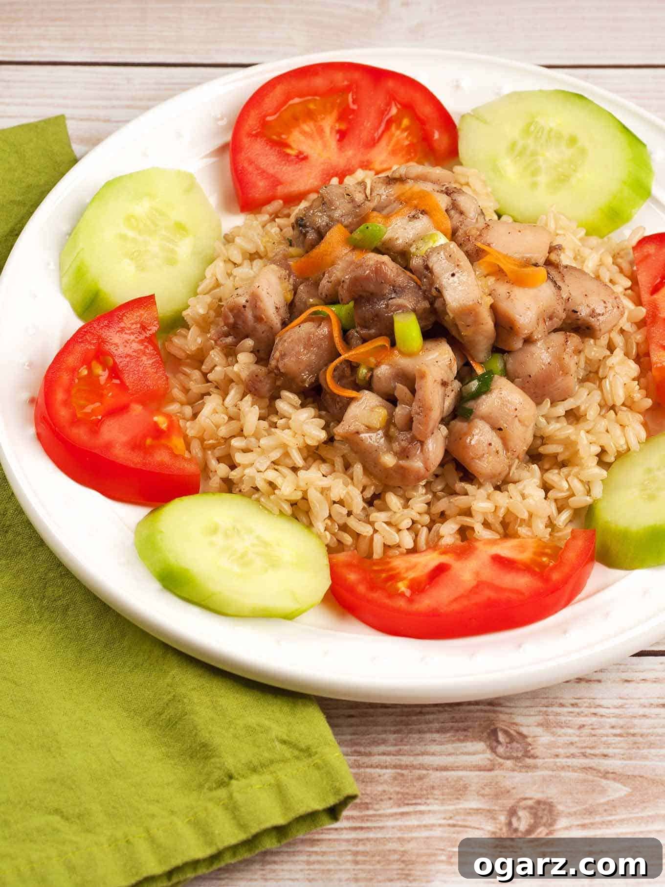 Sticky Ginger Five Spice Chicken 2 Sweet five-spice ginger chicken served over brown rice, garnished with tomato wedges and cucumber slices on a white plate.