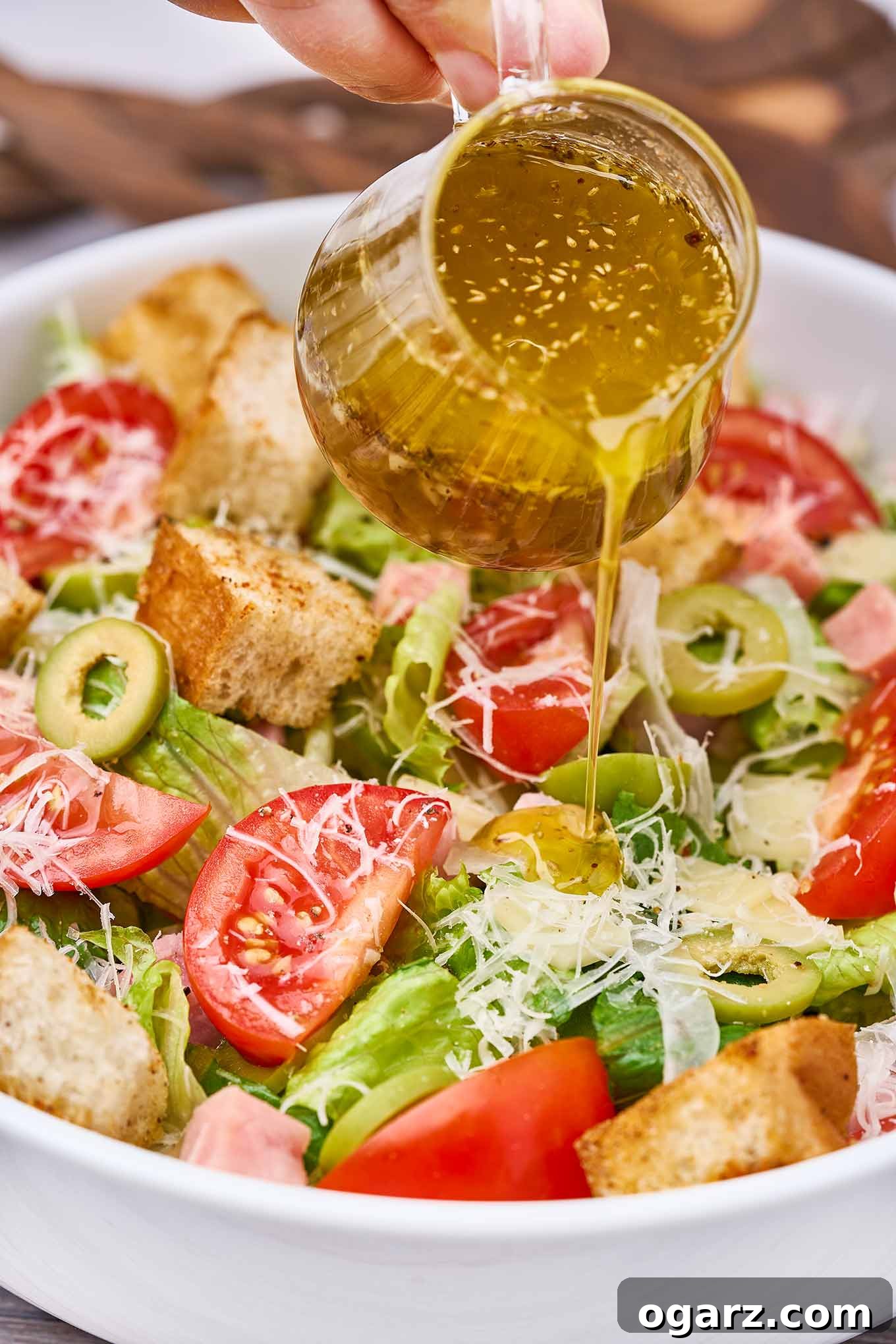 Columbia's Signature 1905 Salad 4 A close up view of dressing being poured over a serving of 1905 salad in a white bowl.