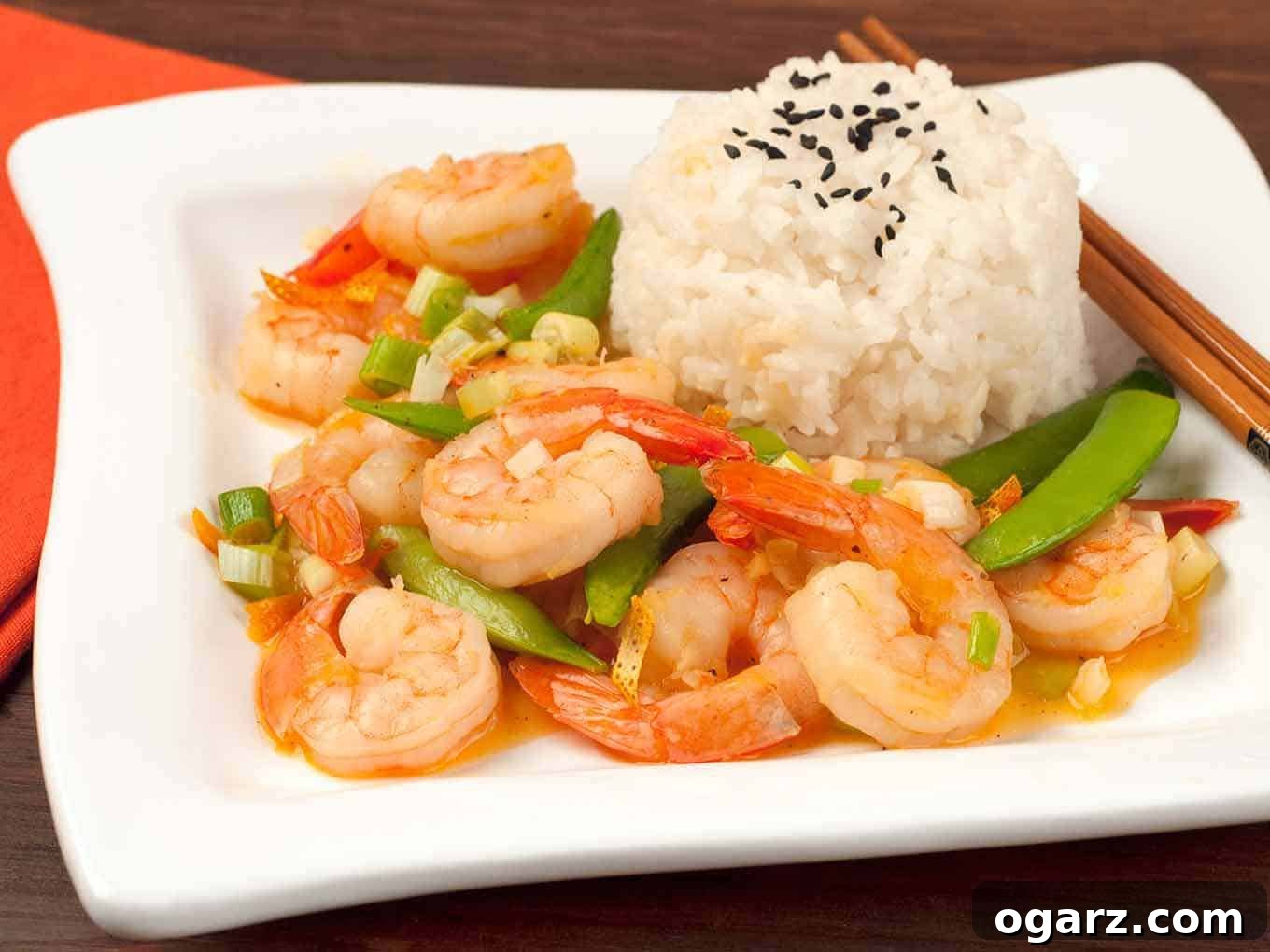 A side view of the beautifully presented stir-fried shrimp with orange peel, snap peas, and scallions, accompanied by white rice sprinkled with black sesame seeds.