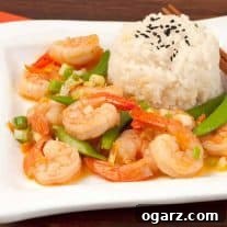 A side view of stir-fried shrimp with orange peel, snap peas, and scallions served with white rice topped with black sesame seeds.