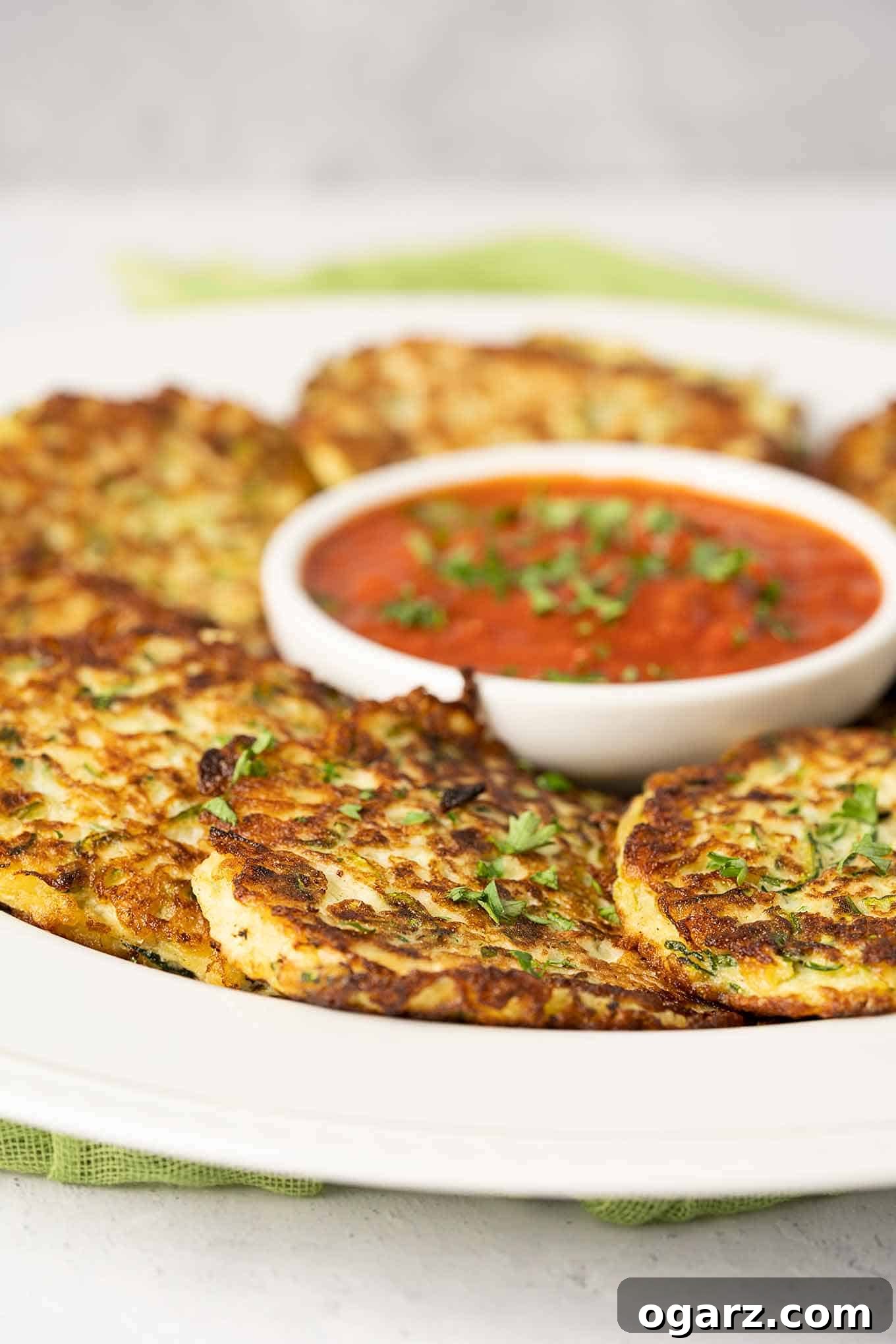 Crispy Parmesan Zucchini Bites 2 A serving platter of freshly made zucchini fritters garnished with chopped parsley and arranged around a small round bowl of marinara dipping sauce.