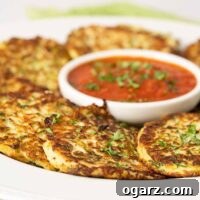 A serving platter of freshly made zucchini fritters garnished with chopped parsley and arranged around a small round bowl of marinara dipping sauce.