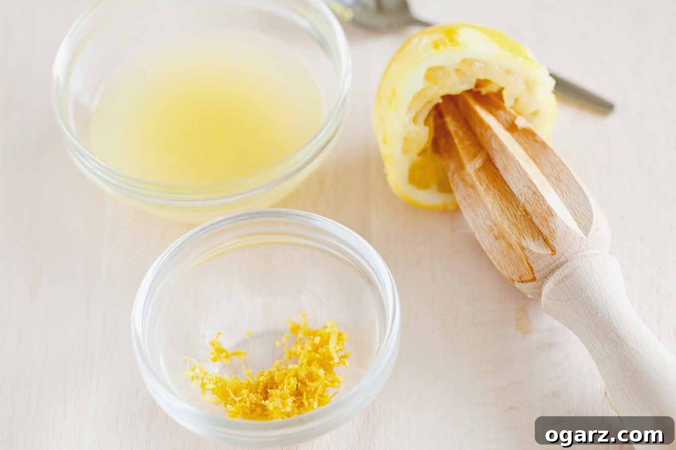 Avgolemono: Velvety Greek Lemon Soup 3 Glass prep bowls filled with freshly squeezed lemon juice and aromatic lemon zest, positioned beside a halved lemon and a lemon reamer. These are key ingredients for authentic Greek egg and lemon (avgolemono) soup.