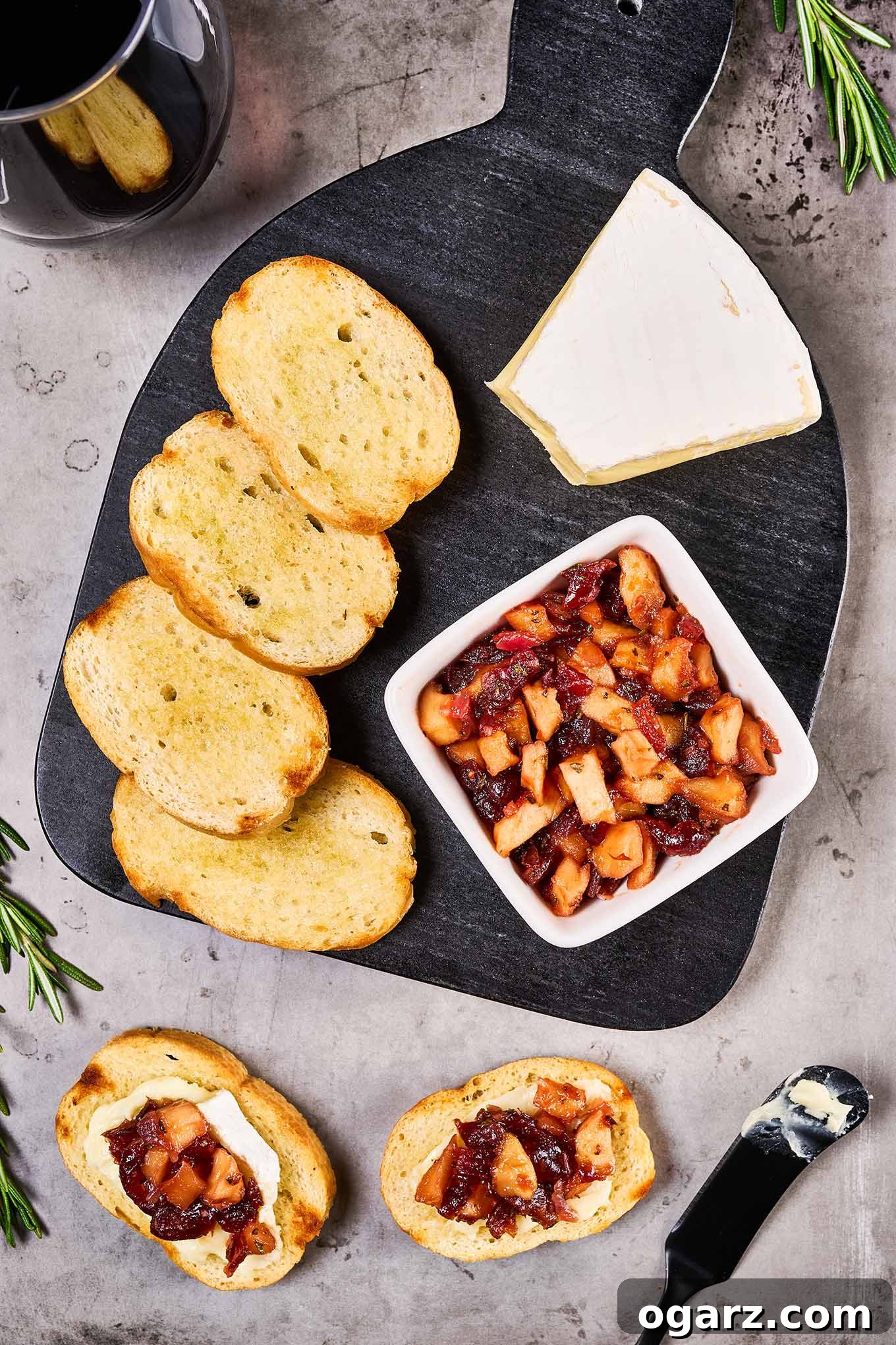 A cheese board with slices of baguette, a wedge of Brie cheese, and a dish of apple cranberry chutney, alongside two prepared cheese and chutney toasts.