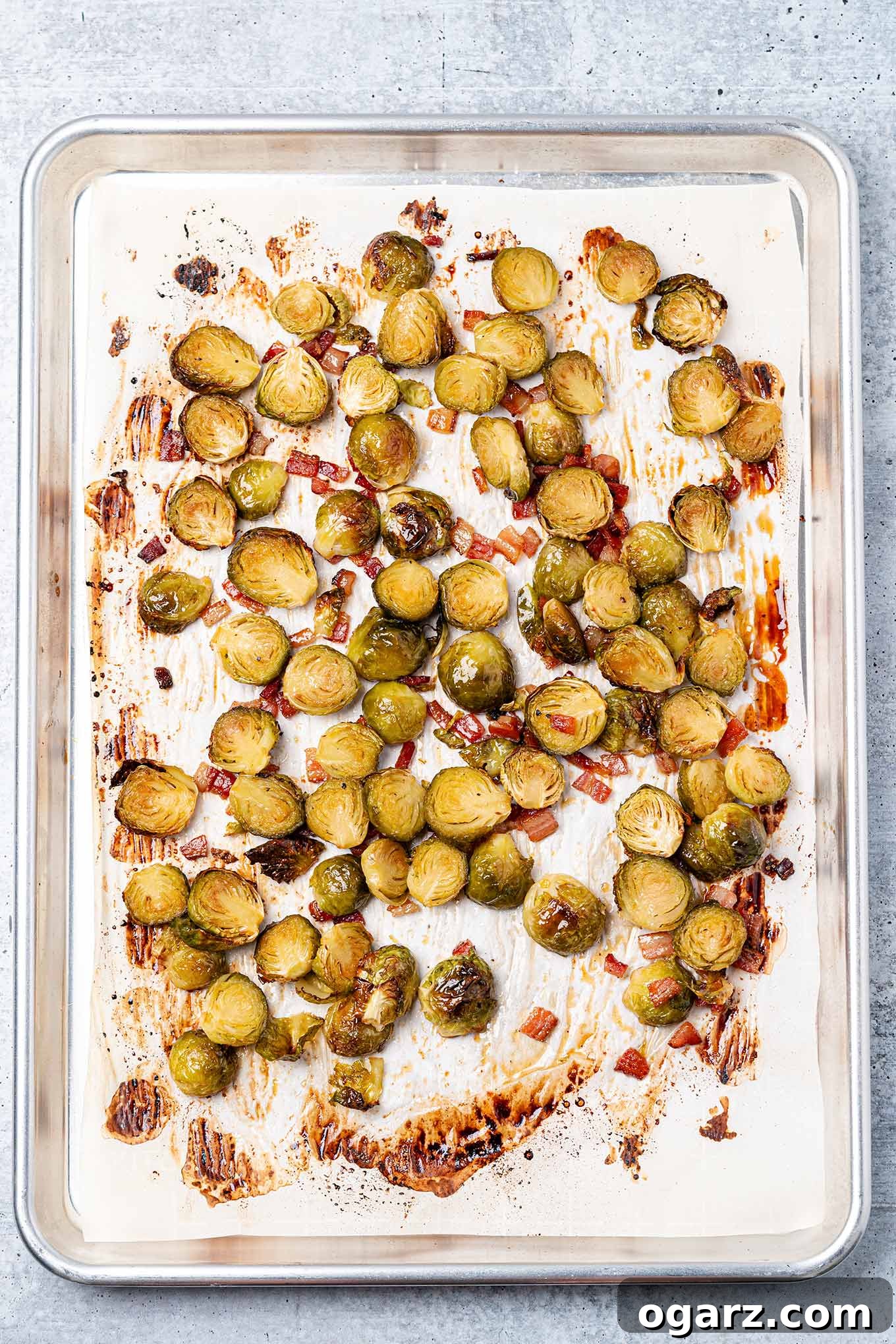 Caramelized Maple Brussels with Crispy Bacon 5 Fully cooked maple glazed Brussels sprouts on a parchment lined baking sheet with bacon bits.