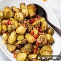 An overhead view of Brussels sprouts glazed in maple syrup and butter with bits of thick-cut bacon in a bowl along with a black serving spoon.