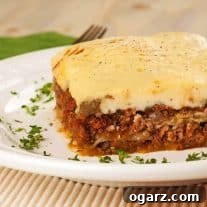 A slice of traditional Greek Moussaka made with ground lamb on a white plate, garnished with chopped parsley.