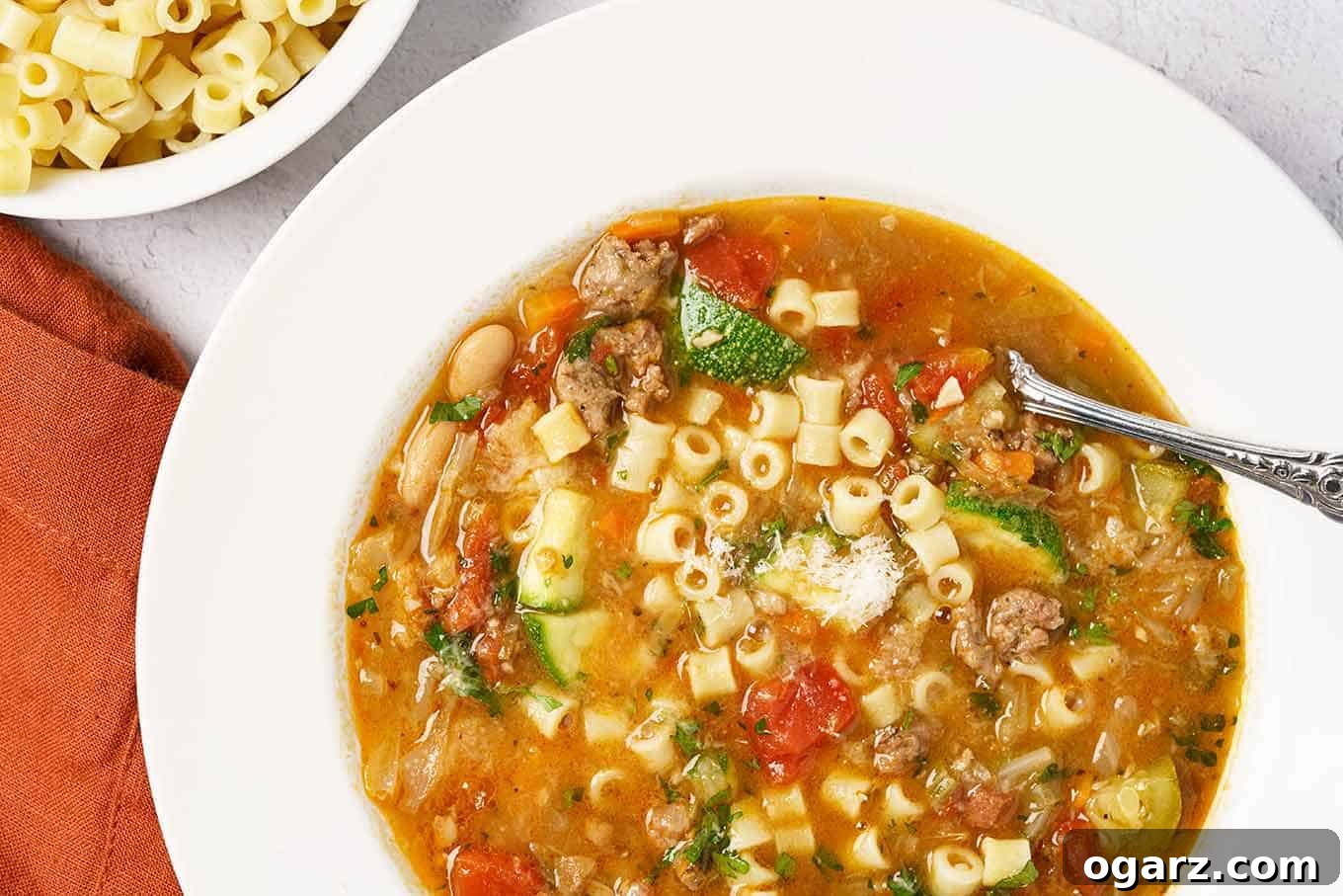 Savory Sausage Minestrone Bowl 4 A close view of homemade minestrone soup with visible chunks of Italian sausage, tomatoes, zucchini, beans, cabbage, carrots, pasta, and more.