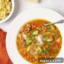 Savory Sausage Minestrone Bowl 5 A bowl of hearty minestrone soup with assorted vegetables and pasta topped with grated cheese, and fresh parsley, ditalini and a wedge of Parmesan on the side.