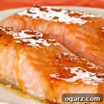 A white serving plate with two oven-roasted salmon fillets topped with orange marmalade and bourbon glaze.
