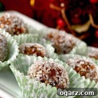 Homemade sugar plums rolled in coarse sugar, arranged in holiday paper candy cups, with festive Christmas decor in the background.