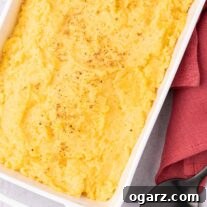 A white, oblong casserole dish of creamy mashed rutabagas sprinkled with nutmeg, a serving spoon and linen napkin on the side.