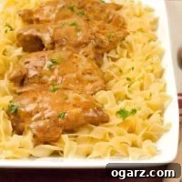 Easy Chicken Paprikas served over a bed of buttered egg noodles, garnished with chopped parsley on a rectangular white platter.
