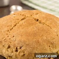 A round, uncut loaf of Irish soda bread on a brown cookie sheet, a green and white tea towel, measuring spoon, and measuring cup in the background.
