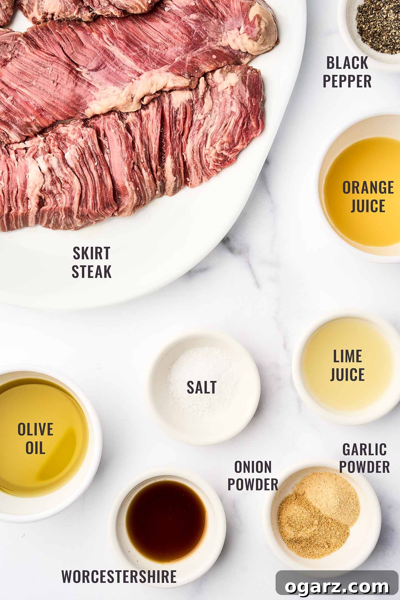 An overhead shot showcasing the key marinade ingredients for grilled skirt steak: raw skirt steak, fresh orange juice, fresh lime juice, olive oil, Worcestershire sauce, garlic powder, onion powder, salt, and black pepper, neatly arranged for preparation.