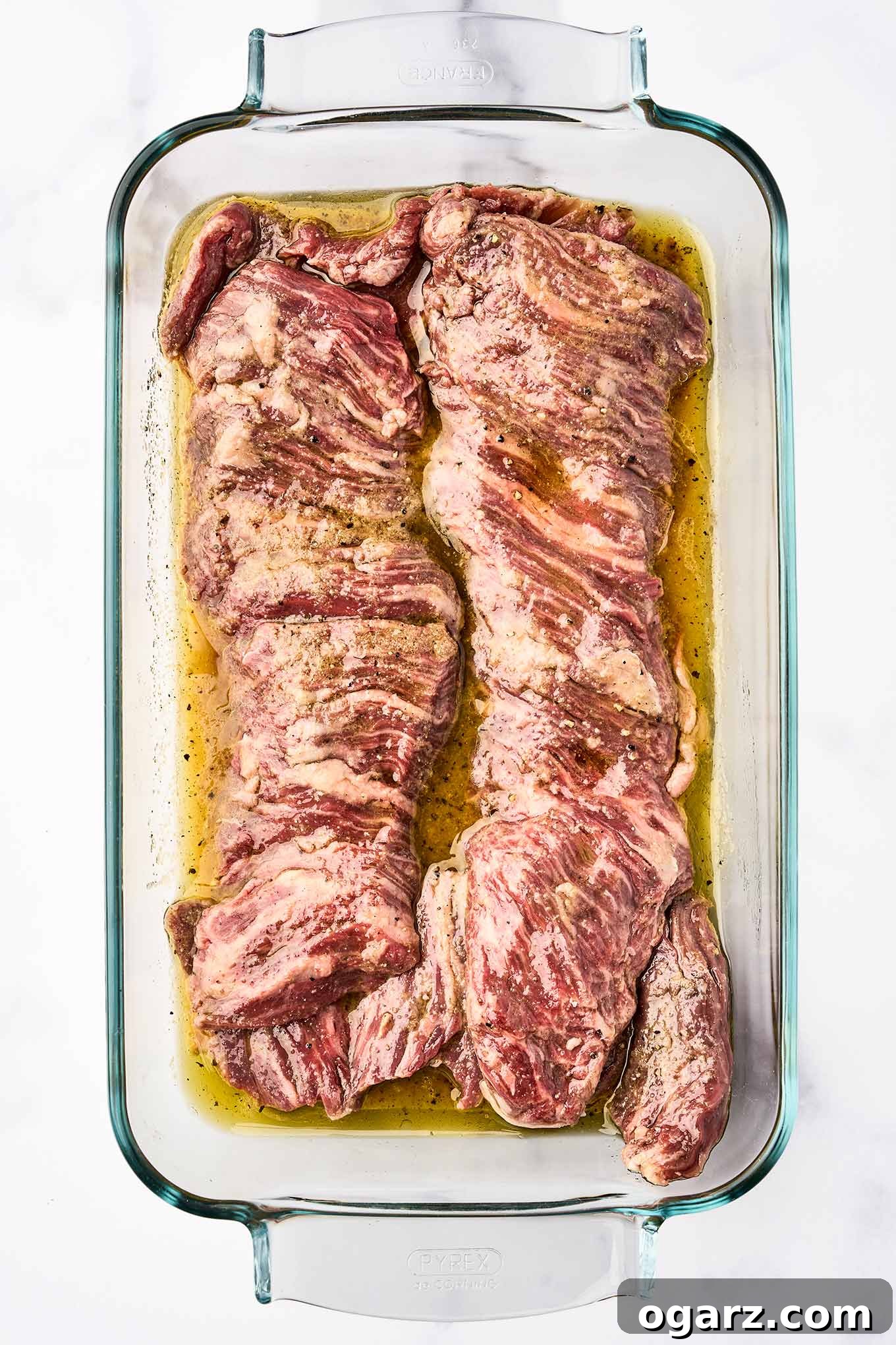 Raw skirt steak marinating in a glass dish with olive oil, orange and lime juice, and seasonings - the first step for making grilled skirt steak with chimichurri sauce.