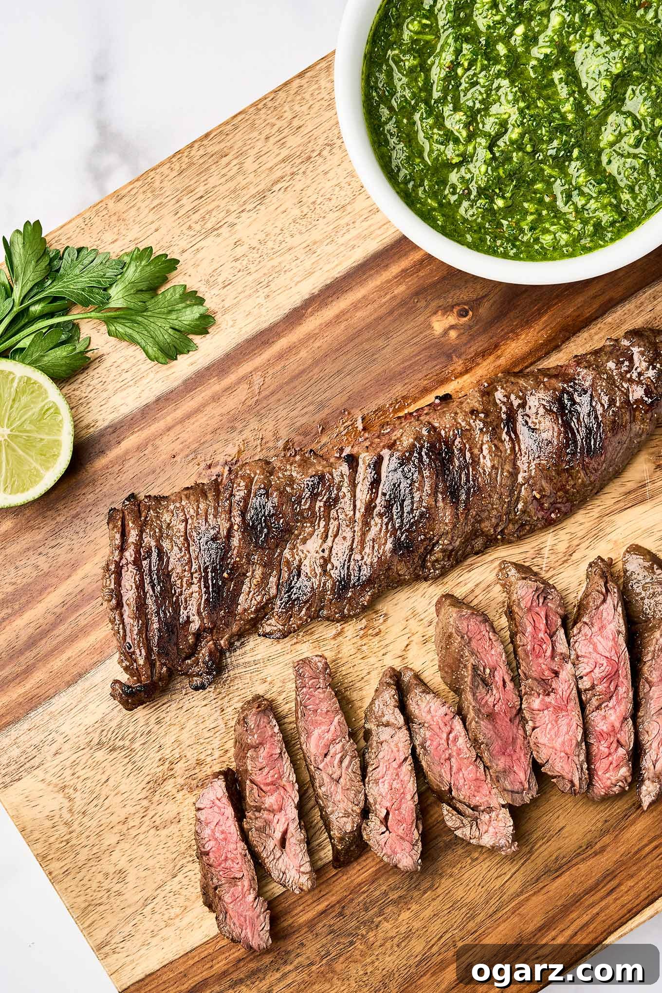 Perfectly grilled skirt steak, partially sliced on a rustic wooden cutting board, with a bowl of vibrant chimichurri sauce ready for serving.