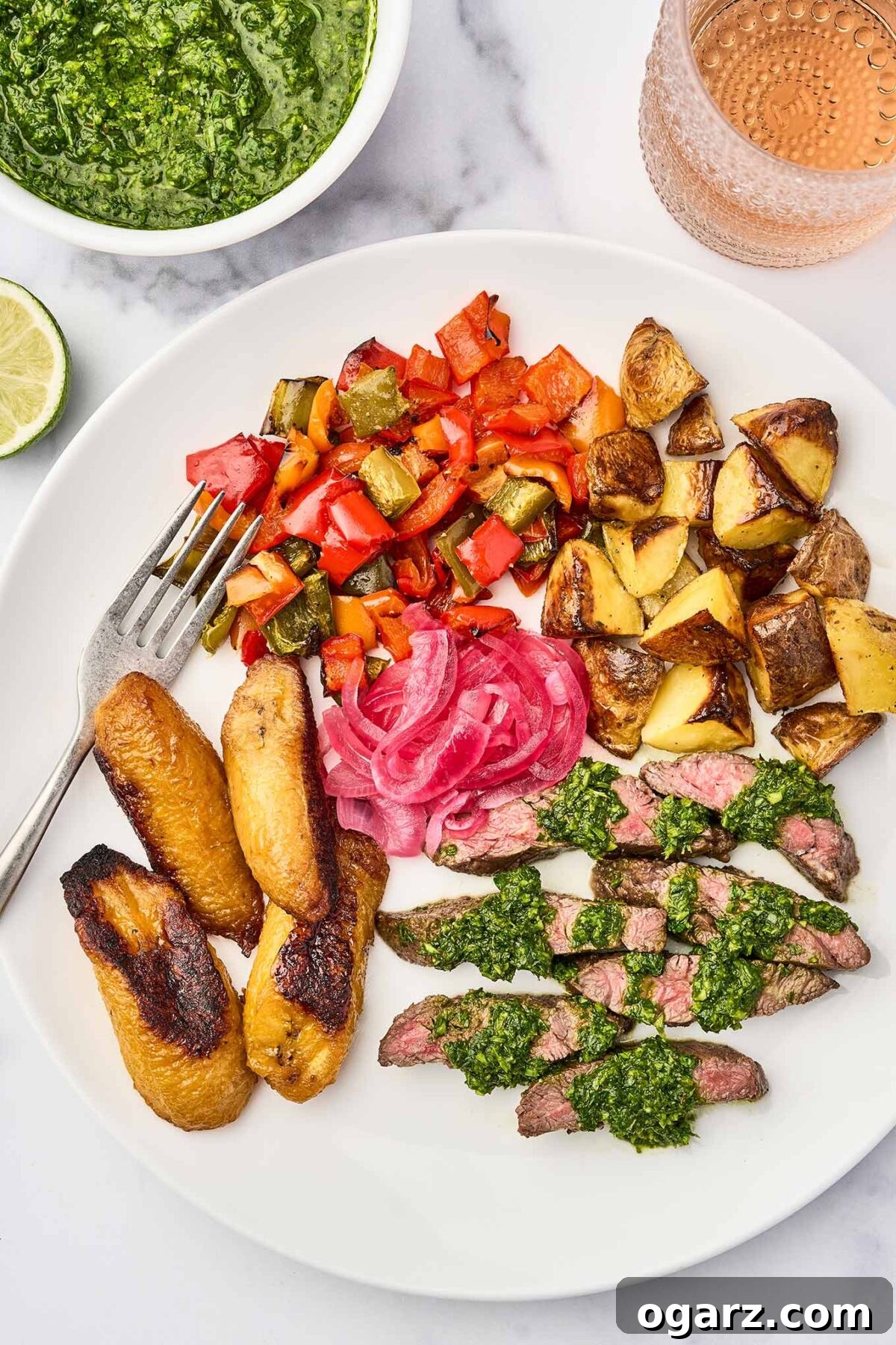 A beautifully presented plate featuring grilled skirt steak with chimichurri sauce, accompanied by roasted sweet plantains, bright pickled red onions, and a medley of roasted potatoes and sautéed bell peppers.