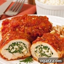 A beautifully plated dish of Spinach and Feta Stuffed Chicken Breasts, covered in Greek-style tomato sauce, ready to be served. Accompanying items include cutlery and a small bowl of feta cheese.