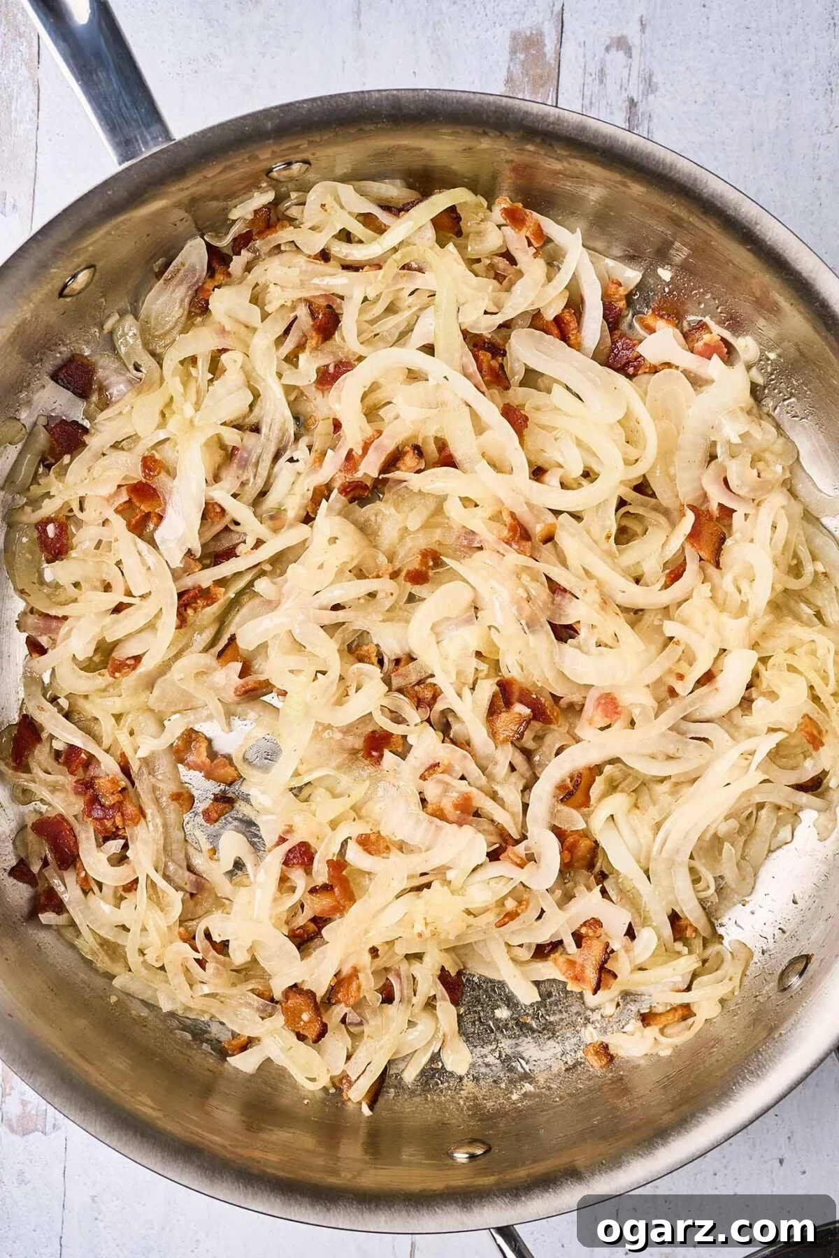 Decadent Blue Cheese Pasta with Crispy Bacon and Sweet Caramelized Onions 4 A large sauté pan containing crispy, thick-cut bacon pieces mixed with thinly sliced sweet onions, which are just beginning the caramelization process, turning a light golden-brown hue.