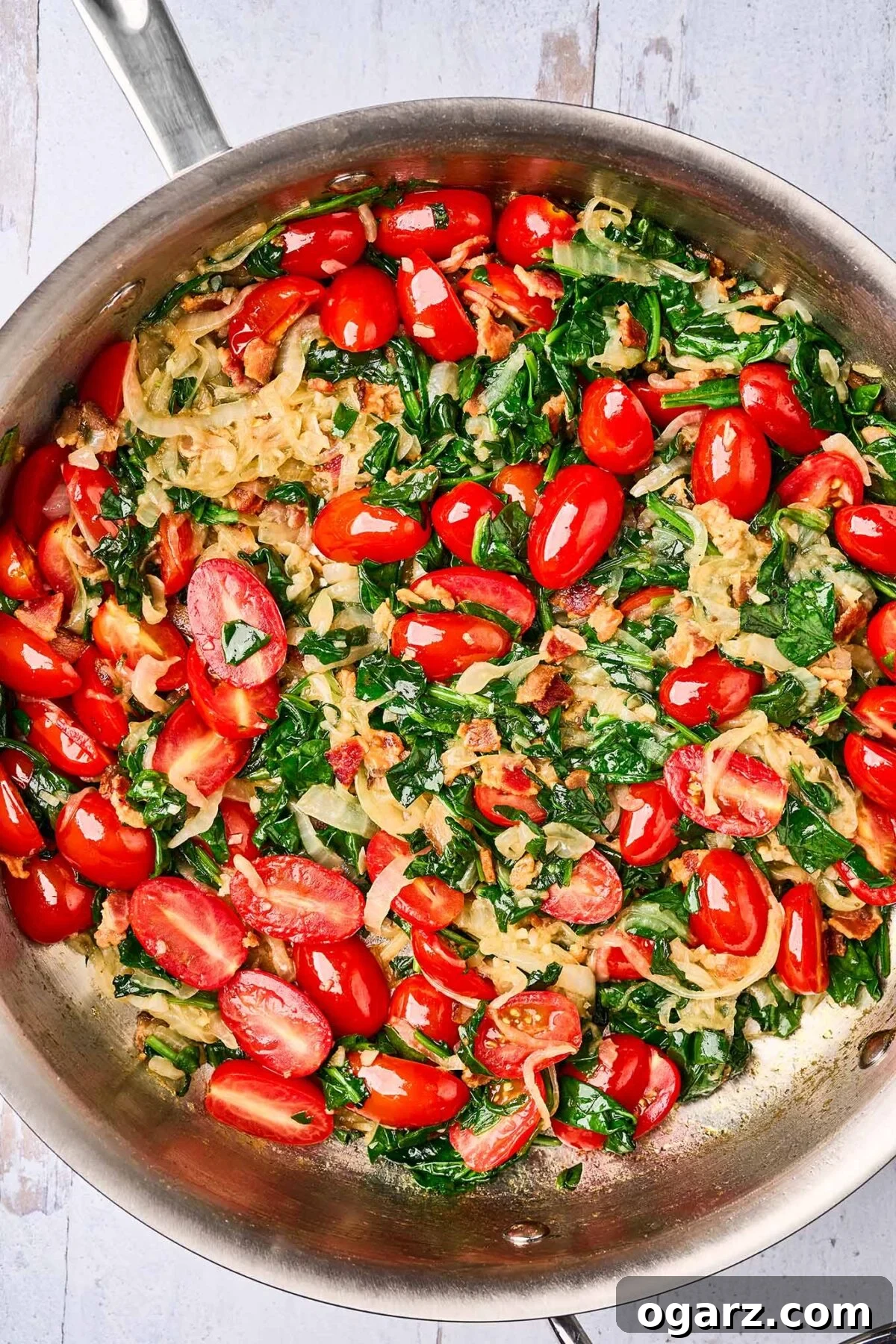 Decadent Blue Cheese Pasta with Crispy Bacon and Sweet Caramelized Onions 5 A sauté pan brimming with a colorful mixture of deeply caramelized onions, crispy bacon, tender sautéed grape tomatoes, and wilted spinach, awaiting the addition of freshly cooked linguine pasta.